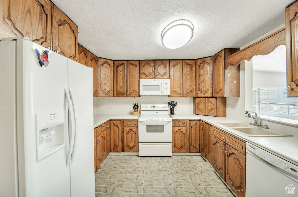Kitchen featuring light countertops, brown cabinetry, white appliances, and a sink