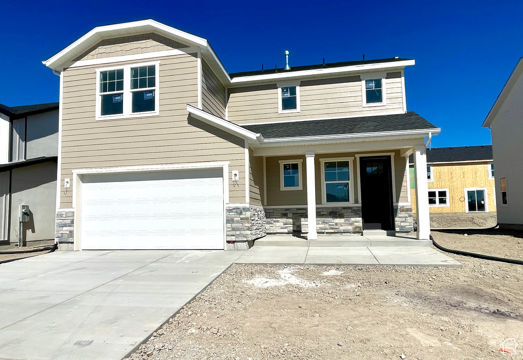 View of front facade featuring covered porch, an attached garage, concrete driveway, and stone siding