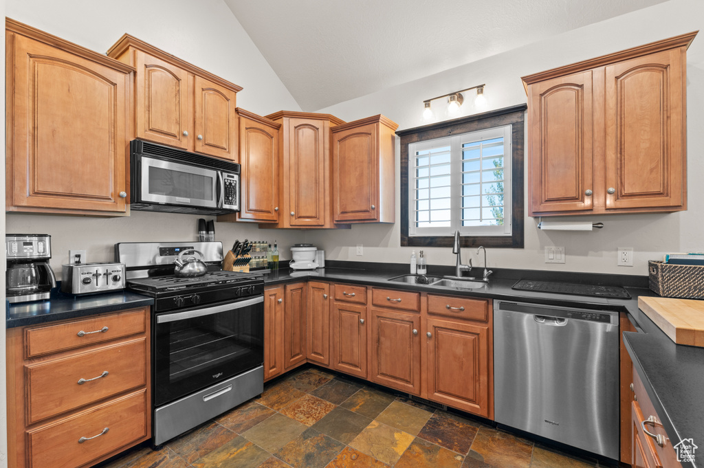 Kitchen featuring a sink, appliances with stainless steel finishes, vaulted ceiling, and dark countertops