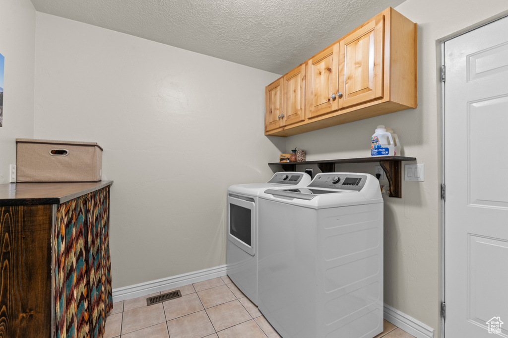 Clothes washing area with visible vents, cabinet space, light tile patterned floors, baseboards, and washer and dryer