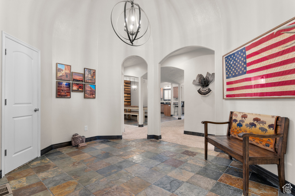 Hallway with stone tile floors, baseboards, a high ceiling, a chandelier, and arched walkways