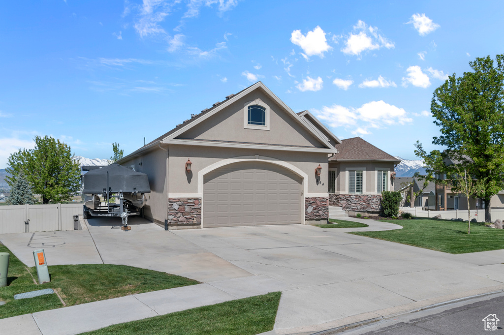 View of front of home featuring fence, an attached garage, stone siding, stucco siding, and a front yard