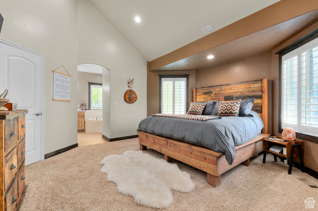 Bedroom with connected bathroom, light carpet, arched walkways, recessed lighting, and baseboards