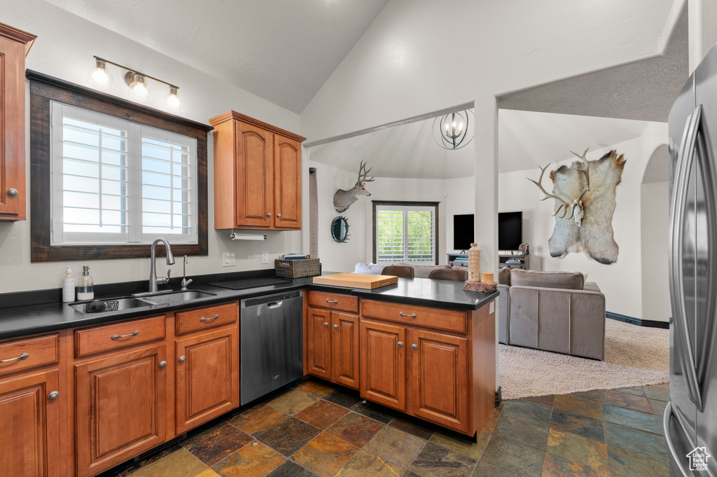 Kitchen featuring dark countertops, a sink, a peninsula, stainless steel appliances, and stone tile floors
