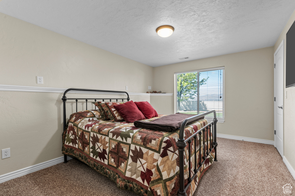 Carpeted bedroom featuring a textured ceiling, baseboards, and visible vents