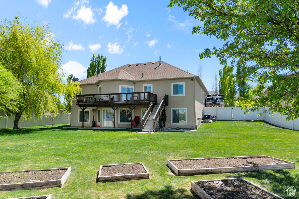Back of property featuring a fenced backyard, a garden, stucco siding, and a deck
