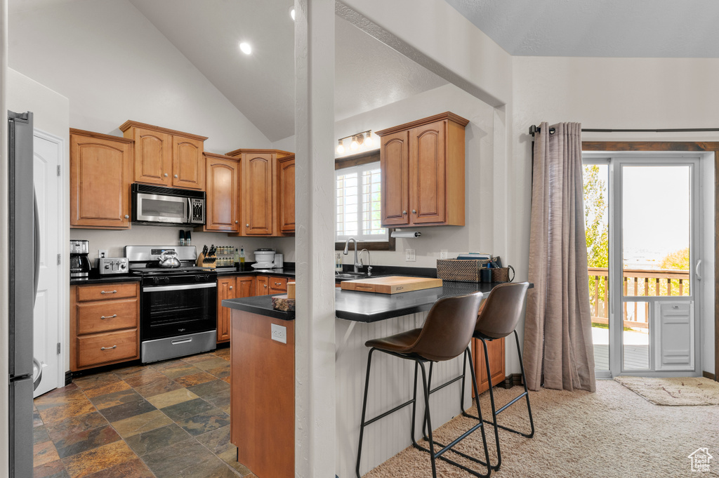 Kitchen with dark countertops, appliances with stainless steel finishes, a breakfast bar, a peninsula, and vaulted ceiling
