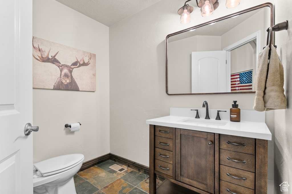 Half bath featuring vanity, visible vents, toilet, baseboards, and stone finish flooring