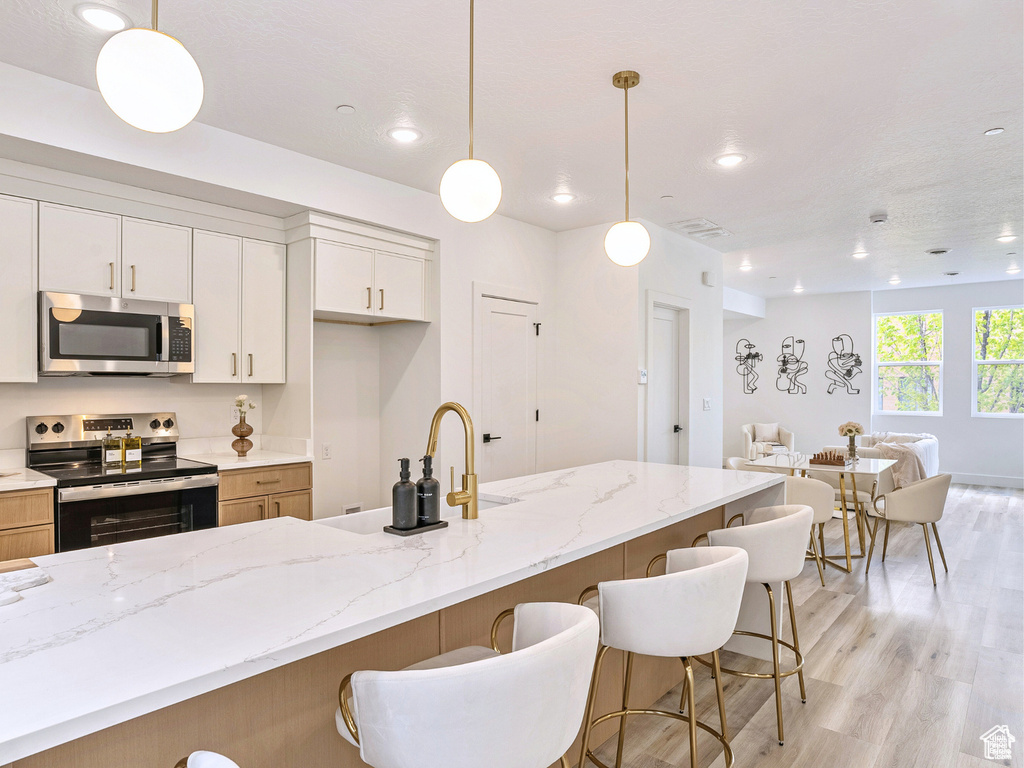 Kitchen with a kitchen breakfast bar, open floor plan, appliances with stainless steel finishes, and light wood-type flooring