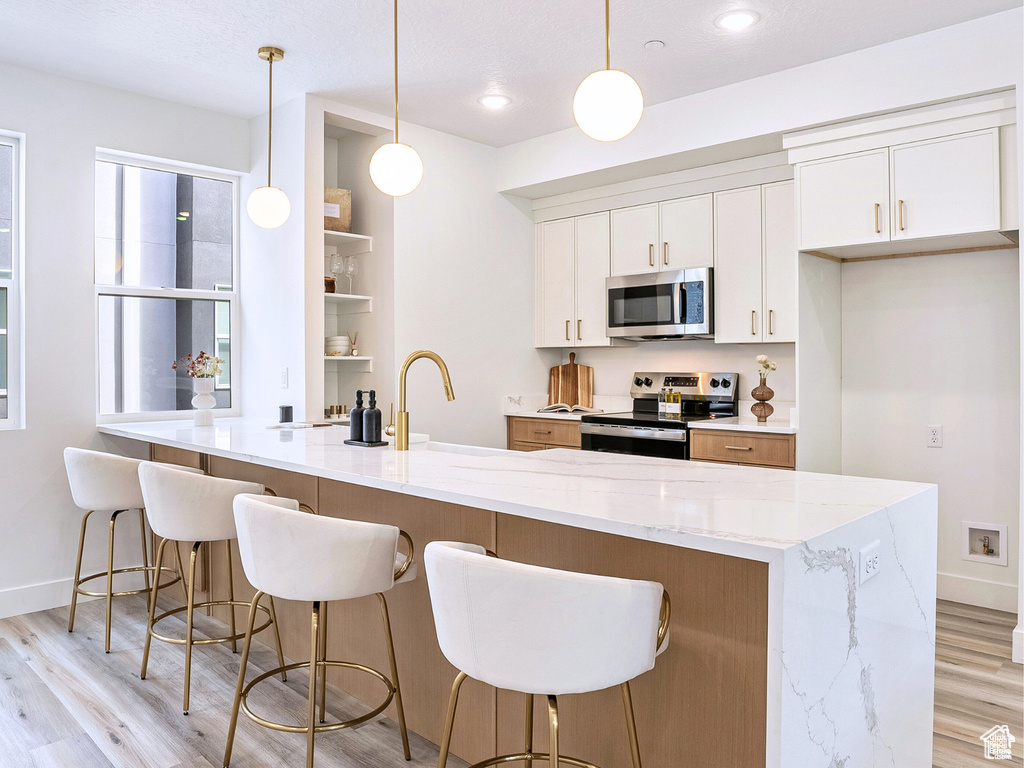 Kitchen featuring white cabinetry, baseboards, appliances with stainless steel finishes, and light wood-type flooring