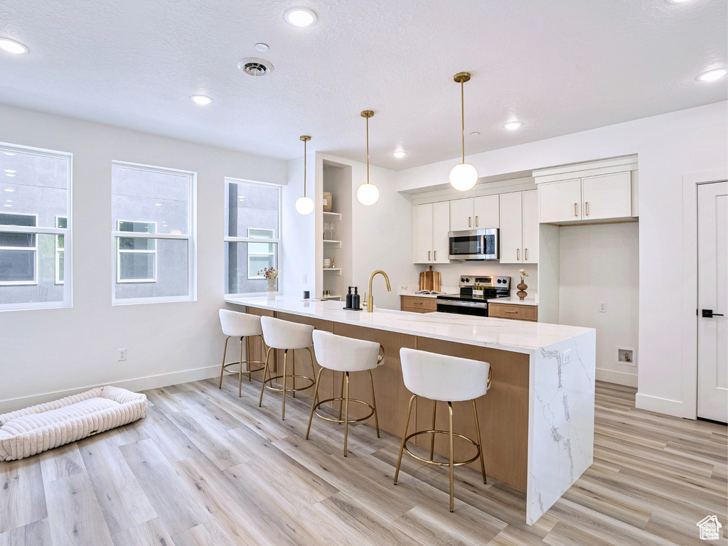Kitchen with a breakfast bar area, stainless steel appliances, a peninsula, and light wood-style floors
