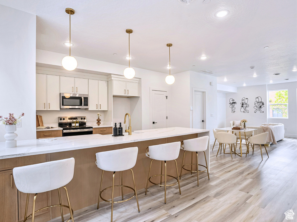 Kitchen featuring a kitchen breakfast bar, white cabinetry, stainless steel appliances, recessed lighting, and light wood-style flooring