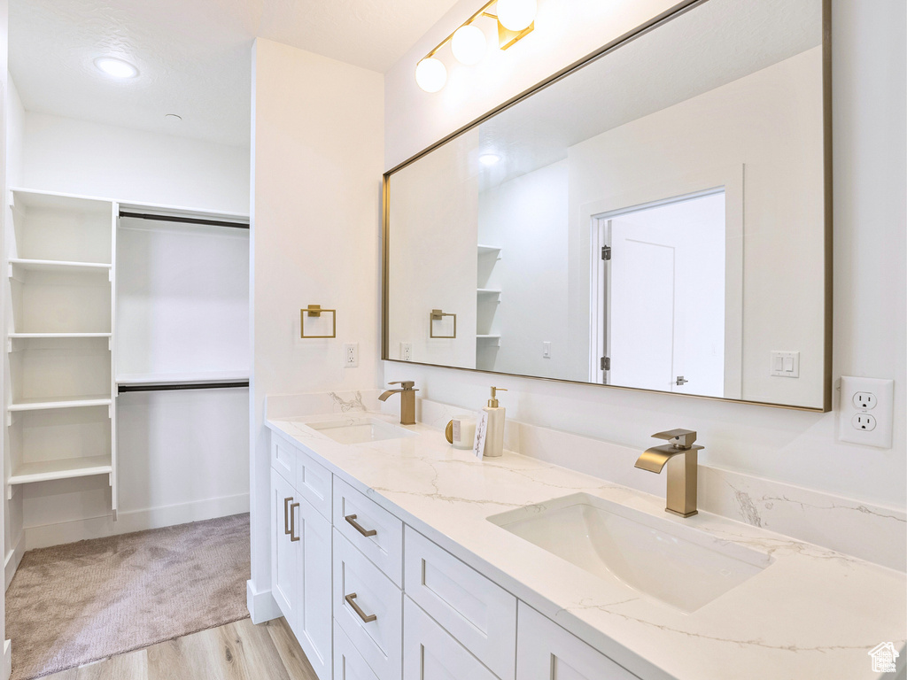 Bathroom with a sink, a walk in closet, double vanity, and wood finished floors