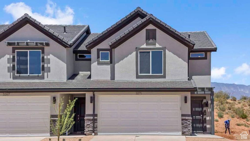 View of front of home featuring a tiled roof, an attached garage, stone siding, and stucco siding