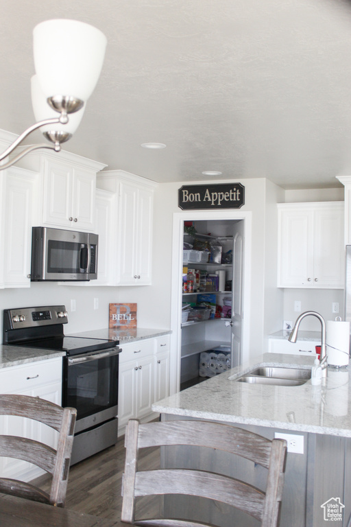 Kitchen with white cabinetry, appliances with stainless steel finishes, a sink, and light stone counters