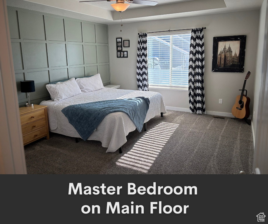 Bedroom featuring carpet, baseboards, a raised ceiling, and a ceiling fan