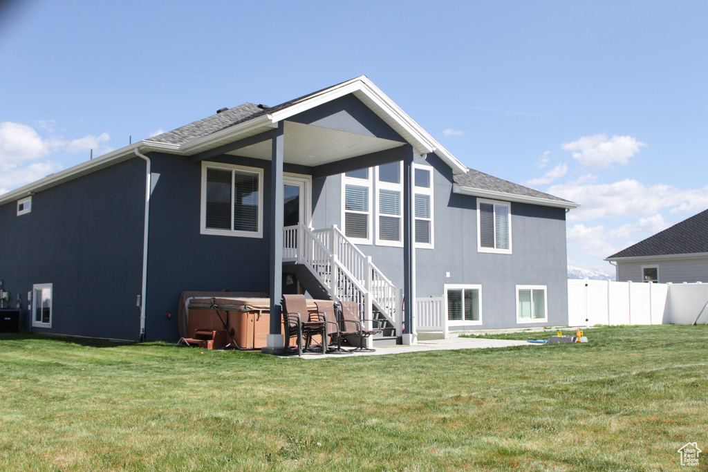 Back of property featuring fence, a yard, a patio, and a hot tub