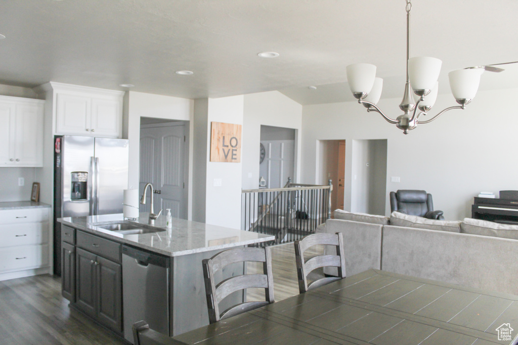 Kitchen with white cabinets, appliances with stainless steel finishes, a sink, a kitchen breakfast bar, and dark wood-style floors