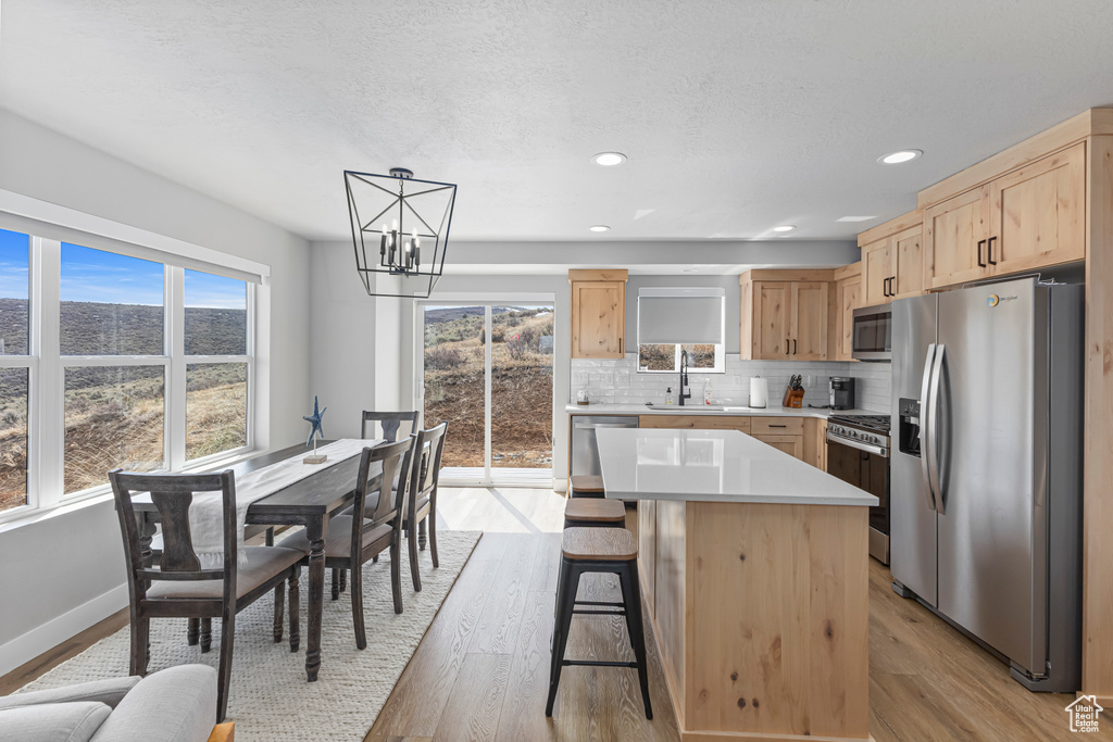 Kitchen with light brown cabinetry, light wood-style floors, a chandelier, a sink, and appliances with stainless steel finishes