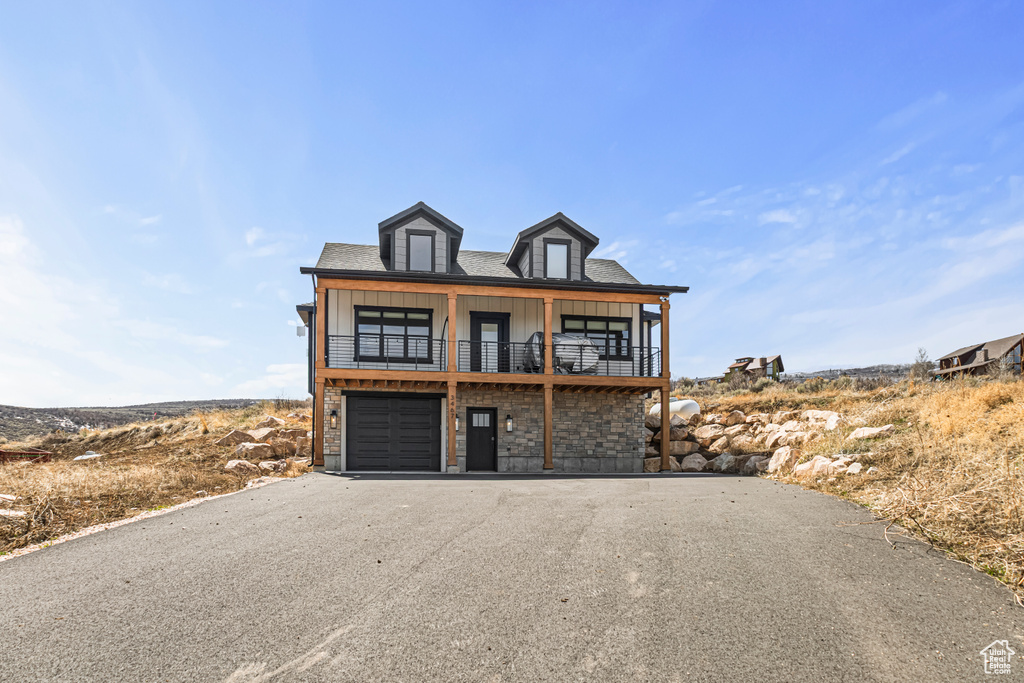 Beach home with board and batten siding, an attached garage, driveway, and a balcony