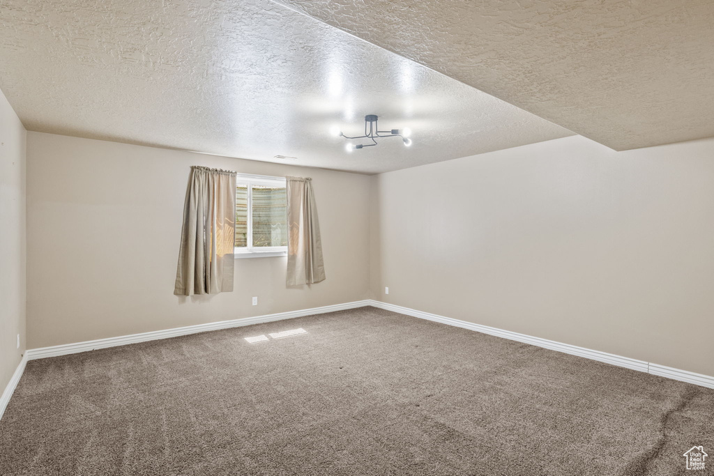 Carpeted empty room with a textured ceiling and baseboards