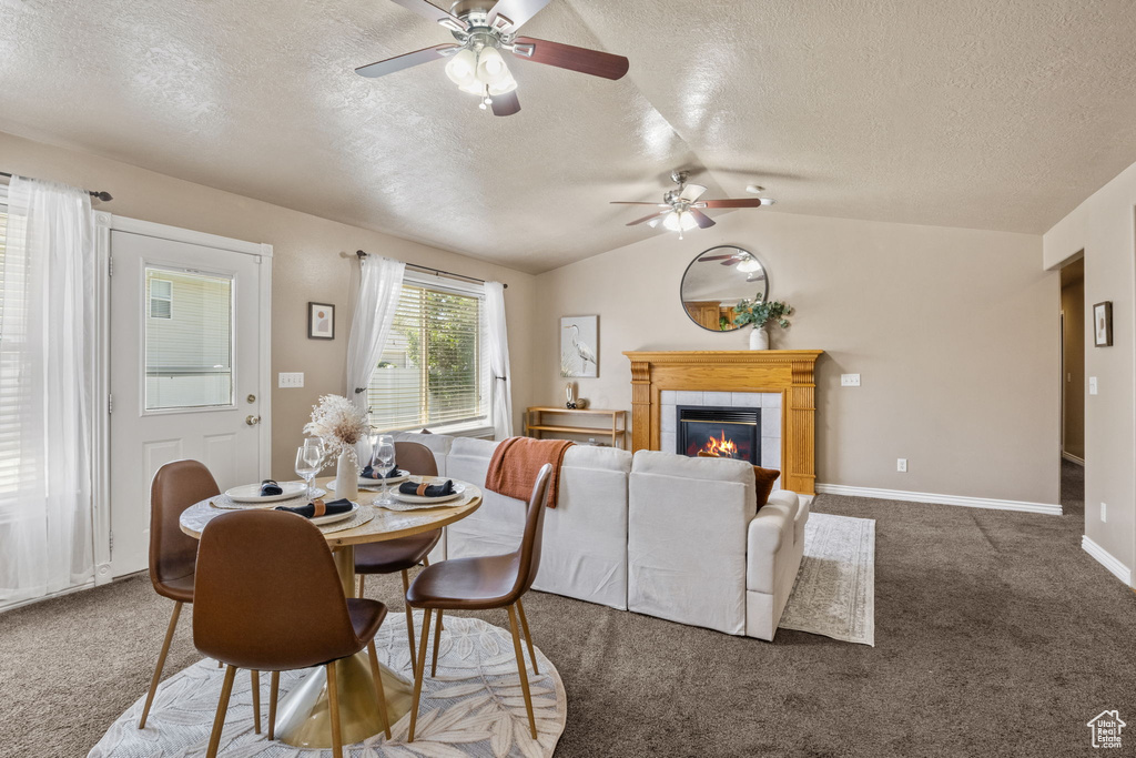 Carpeted dining space featuring a ceiling fan, a textured ceiling, a tiled fireplace, and lofted ceiling