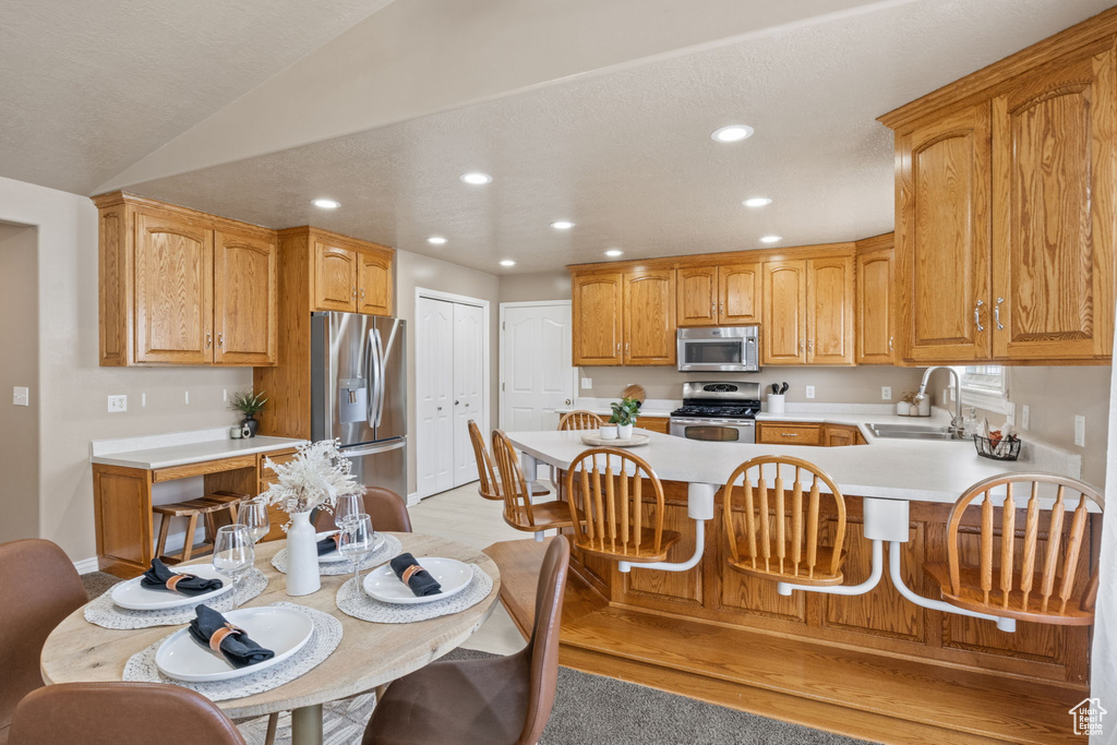 Kitchen with appliances with stainless steel finishes, a sink, light countertops, a peninsula, and recessed lighting