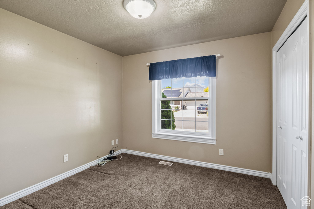 Unfurnished bedroom with a textured ceiling, visible vents, baseboards, a closet, and carpet