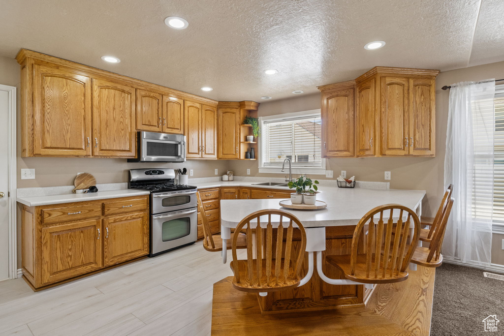 Kitchen with open shelves, appliances with stainless steel finishes, a sink, light countertops, and a textured ceiling