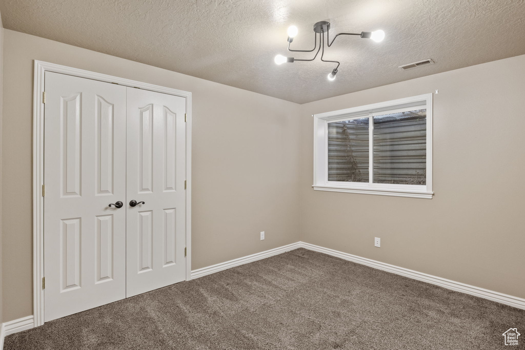 Unfurnished bedroom with a textured ceiling, visible vents, baseboards, a closet, and carpet