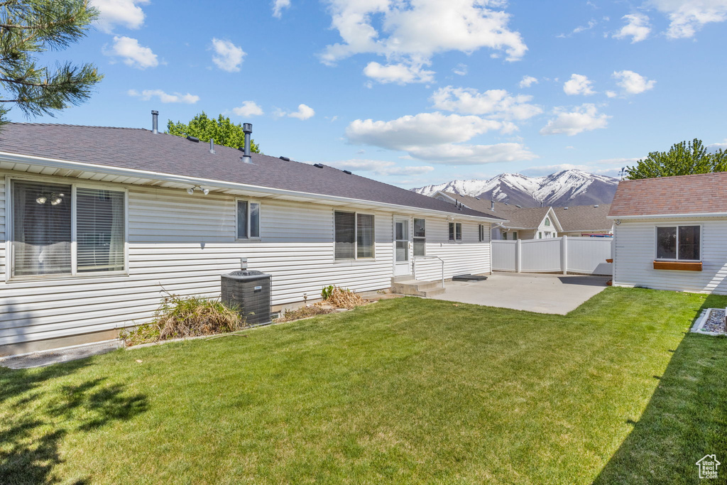 Rear view of house with central air condition unit, a patio, fence, and a lawn