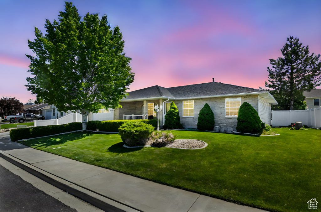 Ranch-style house featuring a shingled roof, fence, and a front yard