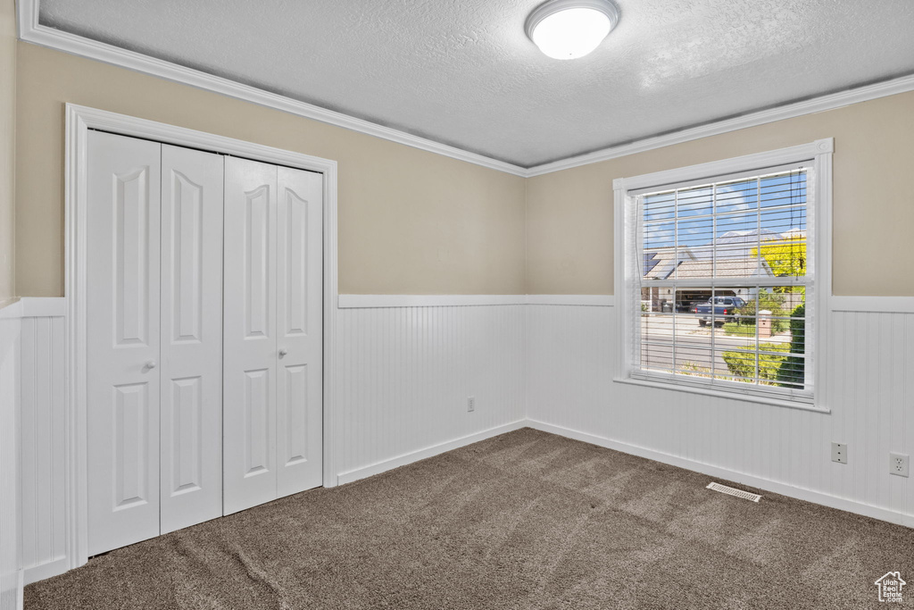 Unfurnished bedroom featuring visible vents, a closet, a textured ceiling, a wainscoted wall, and carpet