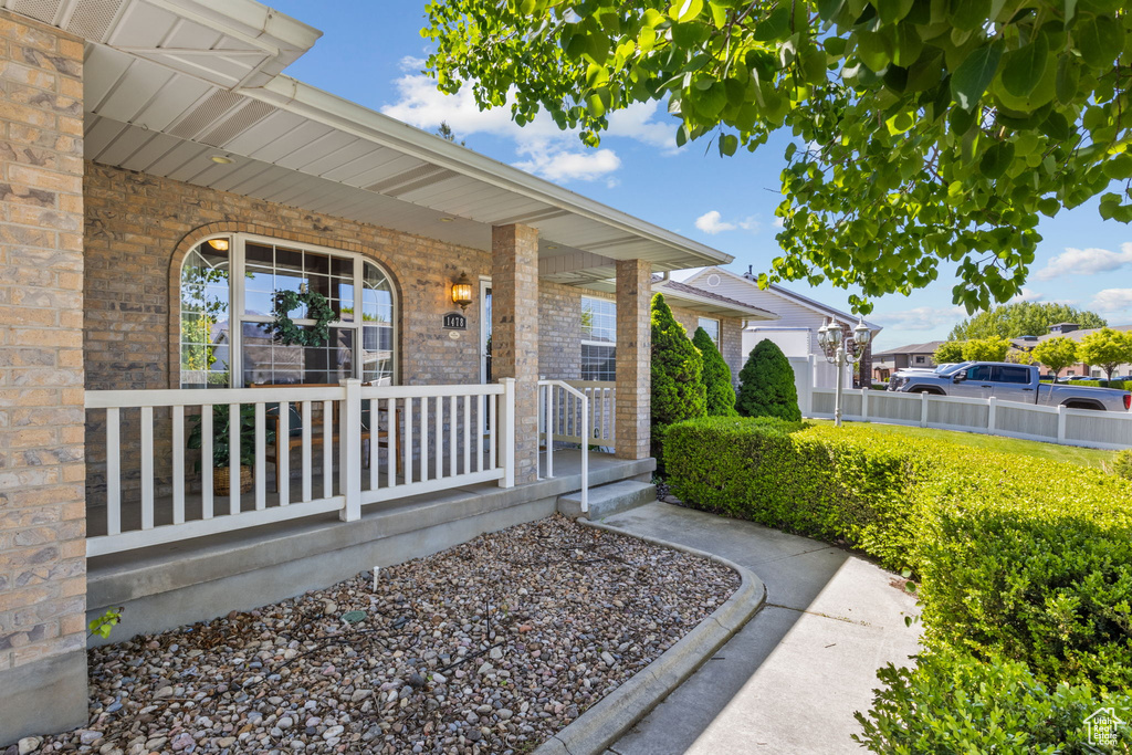 Doorway to property with covered porch, brick siding, and fence