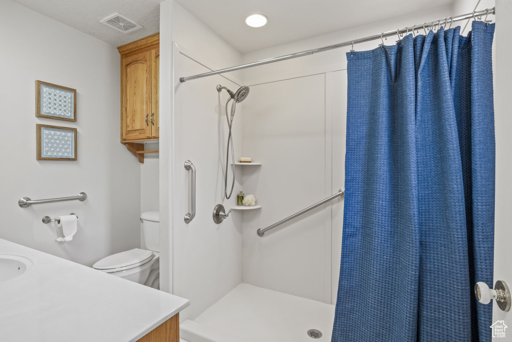 Bathroom with a shower with curtain, vanity, toilet, and visible vents