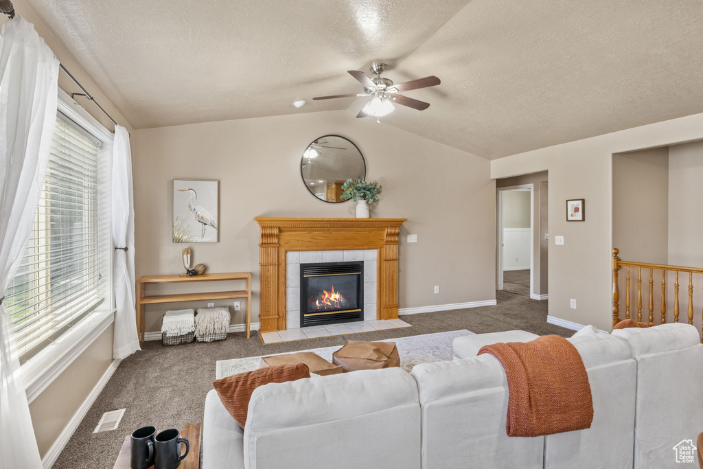 Carpeted living room featuring baseboards, a textured ceiling, a tile fireplace, a ceiling fan, and vaulted ceiling