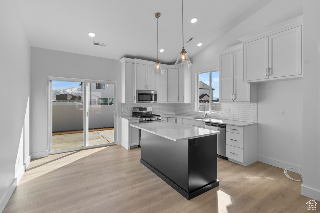 Kitchen featuring a kitchen island, appliances with stainless steel finishes, tasteful backsplash, light countertops, and white cabinets
