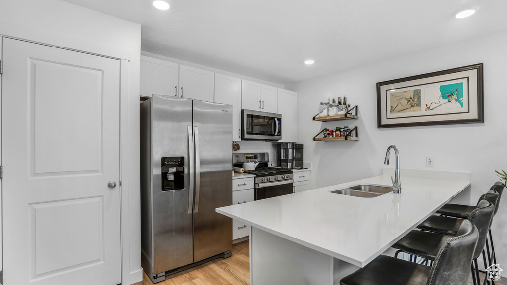 Kitchen featuring a peninsula, a kitchen bar, light wood-type flooring, a sink, and appliances with stainless steel finishes