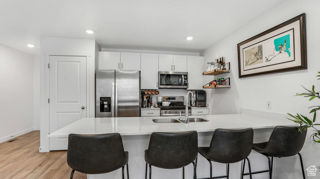 Kitchen with a peninsula, a kitchen bar, a sink, light wood-style flooring, and appliances with stainless steel finishes