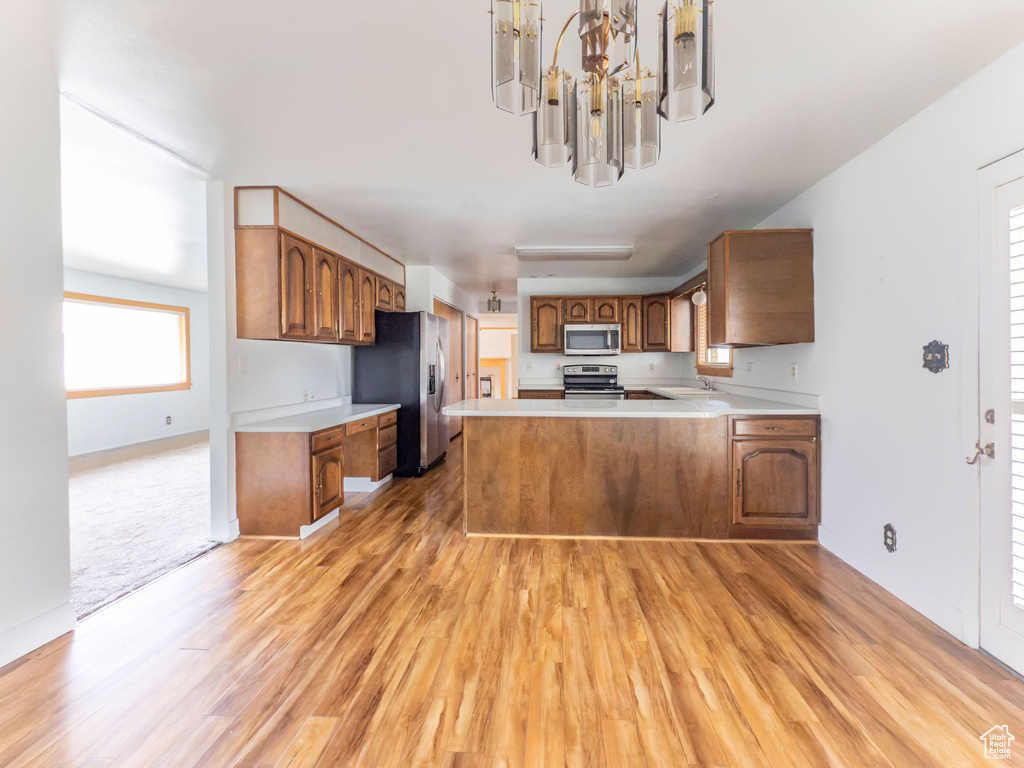 Kitchen with brown cabinetry, appliances with stainless steel finishes, light countertops, light wood finished floors, and an inviting chandelier