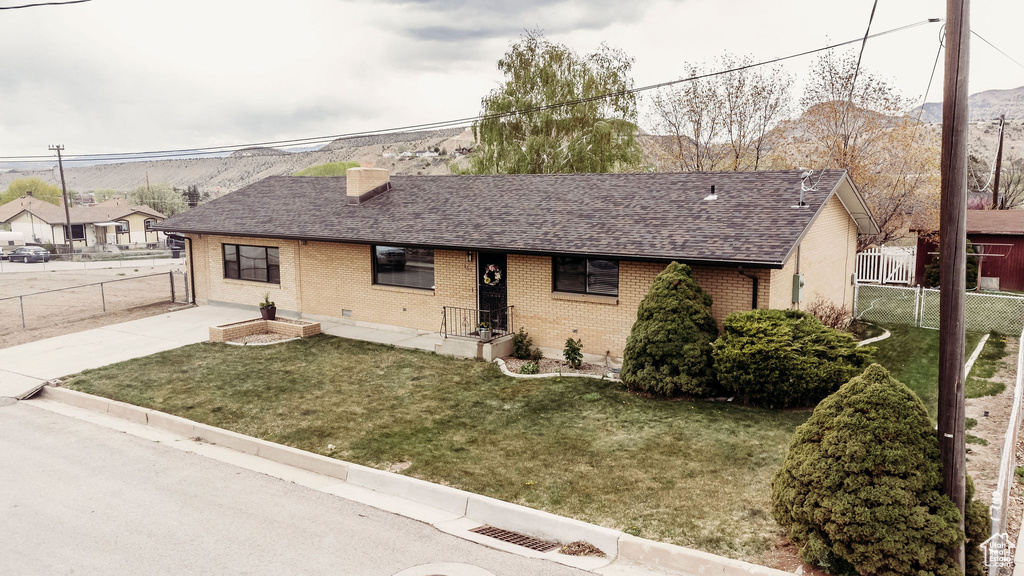 Ranch-style home with a front lawn, fence, a chimney, brick siding, and a shingled roof