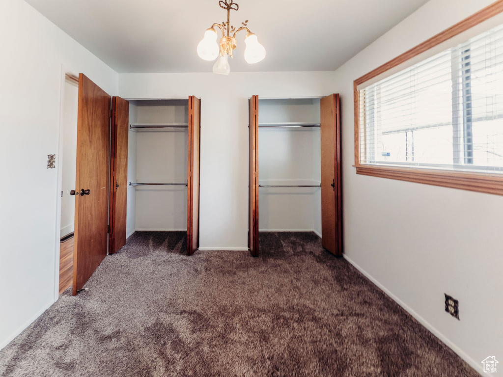Unfurnished bedroom featuring carpet floors, baseboards, two closets, and an inviting chandelier