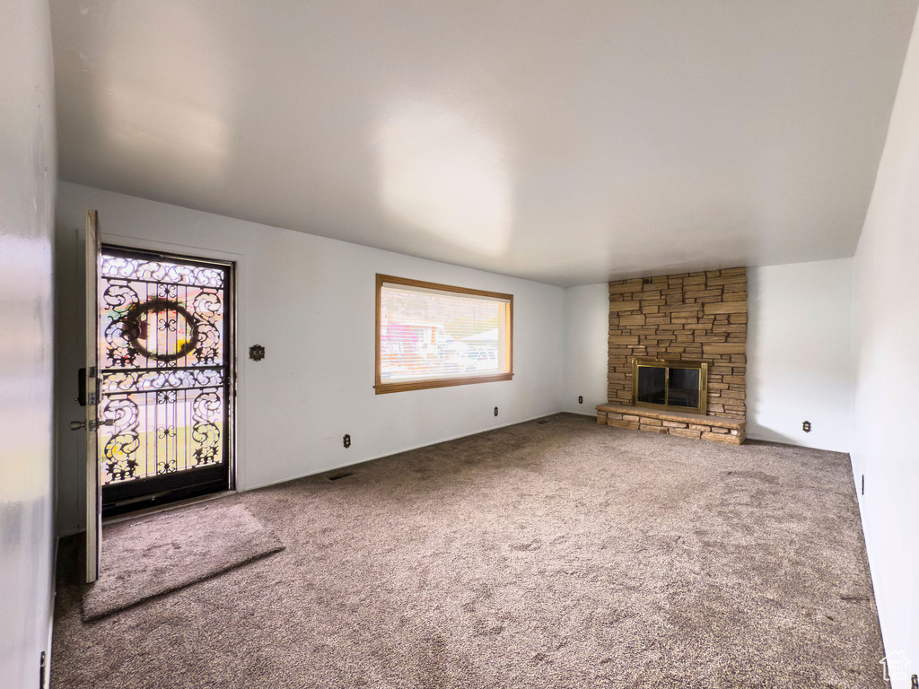 Unfurnished living room with carpet floors and a stone fireplace