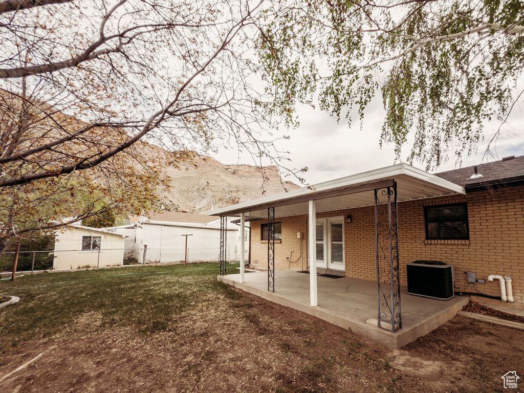 Rear view of property with fence, a patio, brick siding, central AC unit, and a mountain view