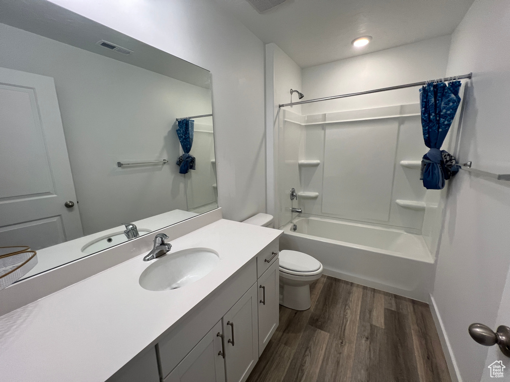 Bathroom with wood finished floors, toilet, vanity, shower / bathtub combination, and baseboards