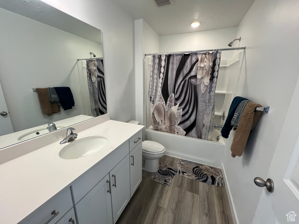 Full bathroom with wood finished floors, toilet, shower / bath combo with shower curtain, and vanity