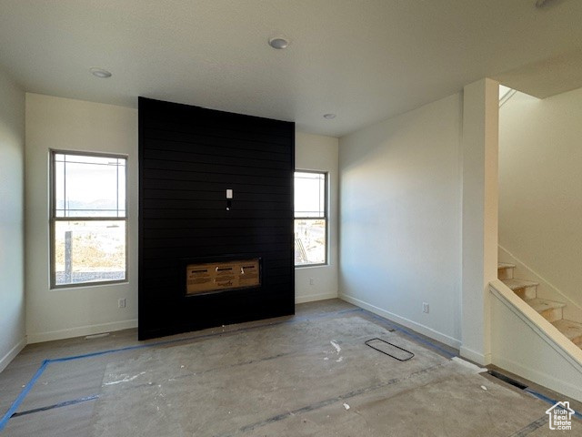 Unfurnished living room with stairway and baseboards