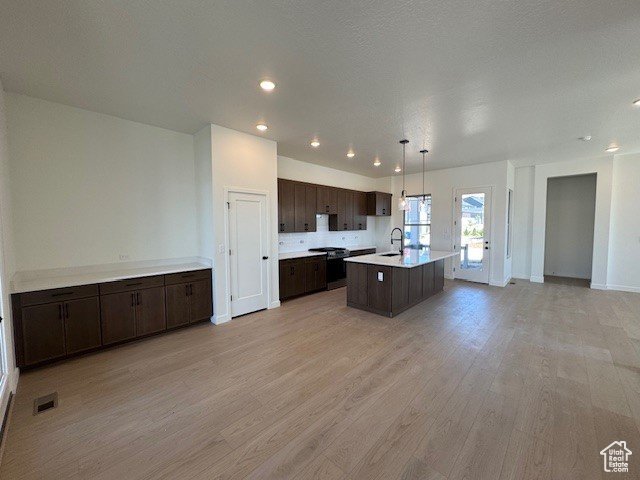 Kitchen featuring open floor plan, dark brown cabinets, range with electric stovetop, light wood-style floors, and a kitchen island with sink