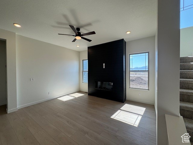 Unfurnished living room with plenty of natural light, stairway, wood finished floors, a ceiling fan, and recessed lighting