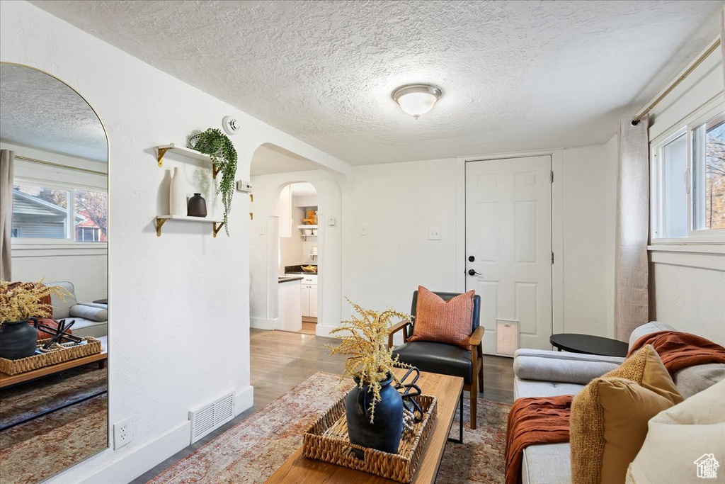 Living room featuring wood finished floors, a textured ceiling, arched walkways, baseboards, and visible vents